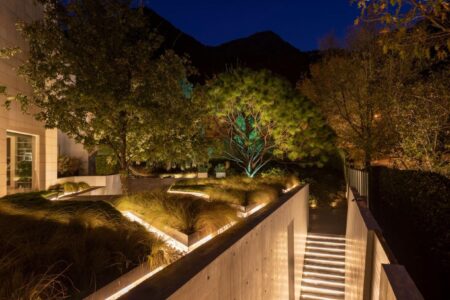 Un camino de concreto se extiende serpenteando a través de un jardín exuberante, iluminado por la cálida luz de las farolas.