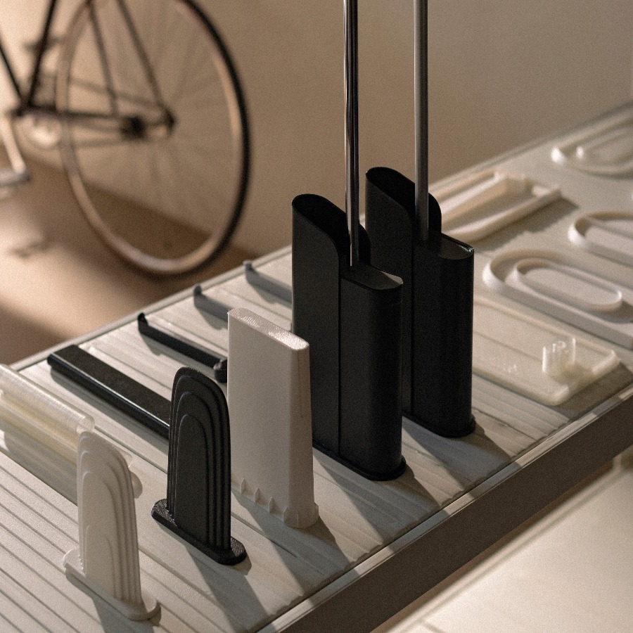 Escobillas de baño negras y componentes impresos en 3D expuestos sobre una mesa, con una bicicleta al fondo.