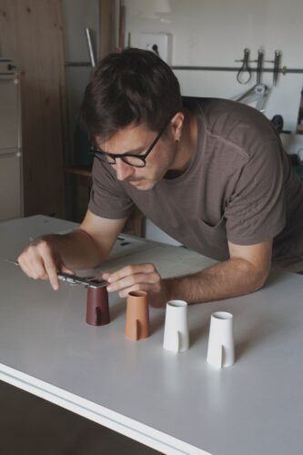 Diseñador midiendo un prototipo con calibre, frente a cuatro piezas de distintos colores sobre una mesa de trabajo.