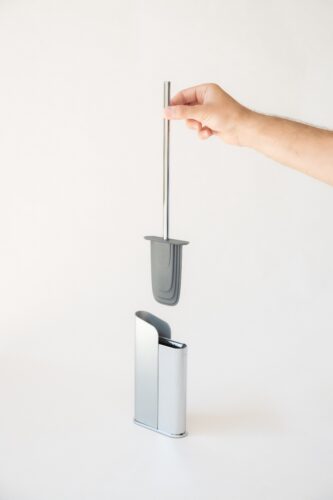 Escobilla de baño de diseño moderno siendo retirada de su soporte metálico por una mano.
