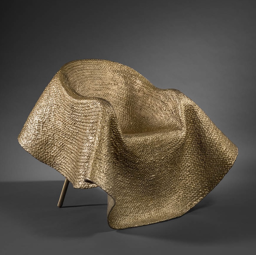 De oro parece. Este sillón escultural forma parte de la serie que el diseñador de moda italiano, Stefano Pilati, ha realizado para la lujosa compañía francesa Pinto. No es de extrañar que quien fue miembro de la dirección creativa de Yves Saint Laurent, Prada o Cerruti ahora nos sorprenda con su implicación en el mundo del mueble. Pilati desarrolla este trabajo a partir de una alfombra de bronce con apariencia de fibras naturales, construida mediante la técnica de fundición a la cera perdida y cosida sobre un sillón de mimbre. La inspiración y su envolvente de gran tamaño vienen del drapeado y otras siluetas que se le ocurrieron cuando cubrió algunos enseres viejos con cojines, paja y yute en su casa de Sicilia. “Aunque no es lo mismo diseñar una prenda que diseñar mobiliario”, nos dice, “hay afinidades con el aspecto industrial del diseño de moda, pues también en él se hace necesario recordar la física, las proporciones y las tensiones compartidas entre las partes”. De ahí que su obra se erija como una escultura muy couture en desafío con la gravedad.
